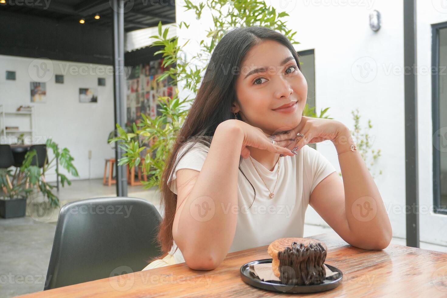 giovane asiatico donna Tenere e mostrando un' nero piatto di ciambella Pasticcino di nome cromboloni con cioccolato Riempimento per merenda volta, sorridente con un' contento e allegro espressione foto