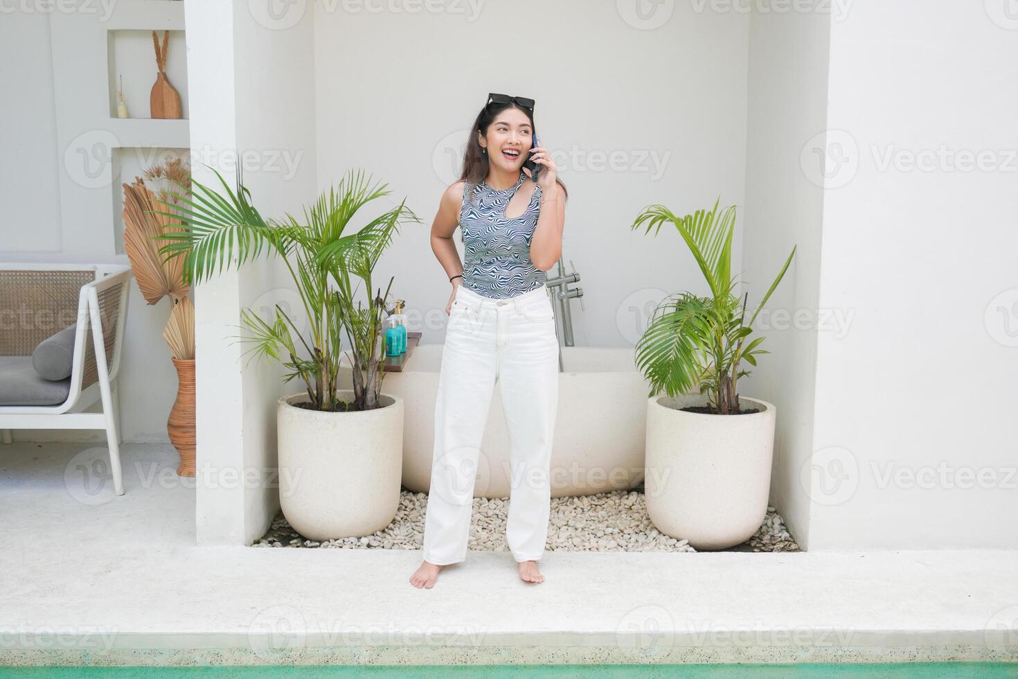 contento asiatico donna in piedi di il piscina mentre chiamata e parlando su un' mobile Telefono con un' allegro Sorridi su il viso foto