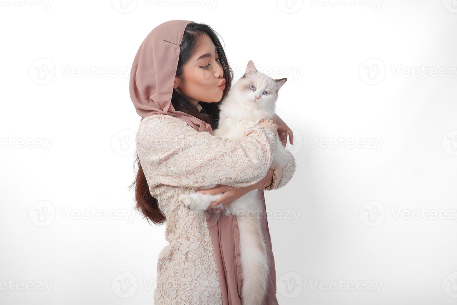 attraente giovane asiatico musulmano donna nel velo hijab sorridente mentre in posa e abbracciare un' bianca bambola di pezza gatto animale domestico foto