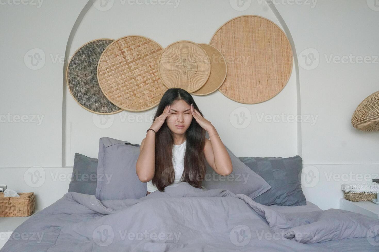 asiatico donna veglia su nel il mattina sensazione stressato e ottenere mal di testa dopo in profondità dormire, ancora sensazione stanco e assonnato restare seduta su letto nel il Camera da letto foto