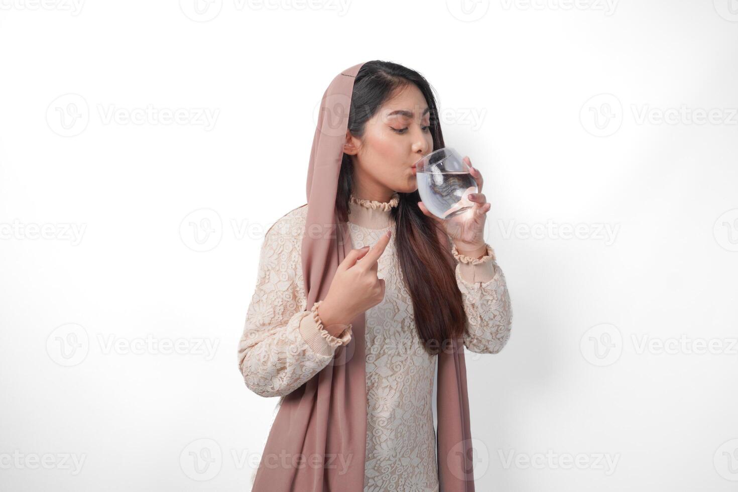 giovane asiatico musulmano donna indossare foulard velo sensazione assetato e potabile acqua dopo digiuno, isolato di bianca sfondo. Ramadan concetto foto