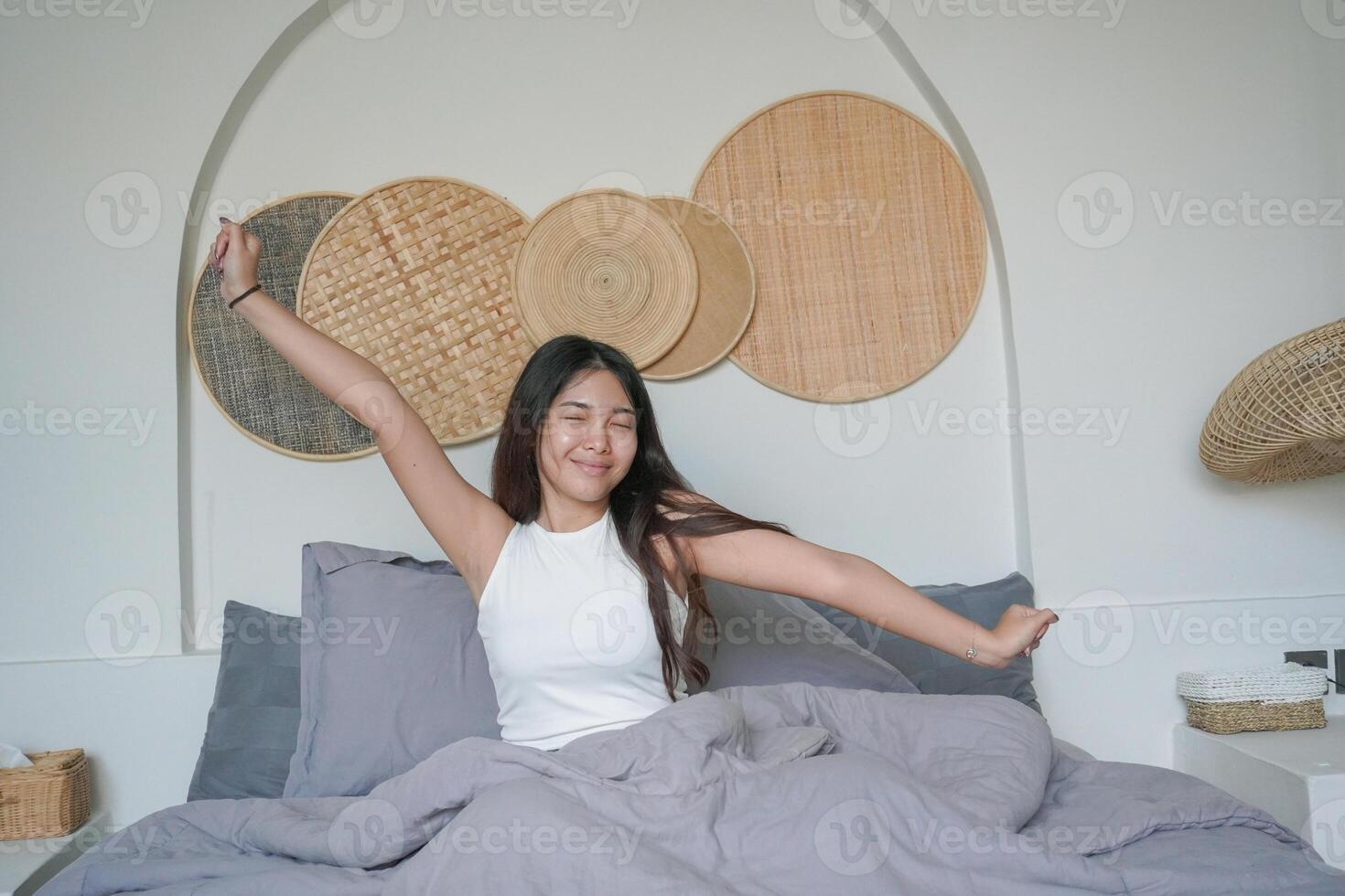 bellissimo asiatico donna veglia su a partire dal dormire dire bugie su letto nel Camera da letto, allungamento mani e sorridente felicemente foto