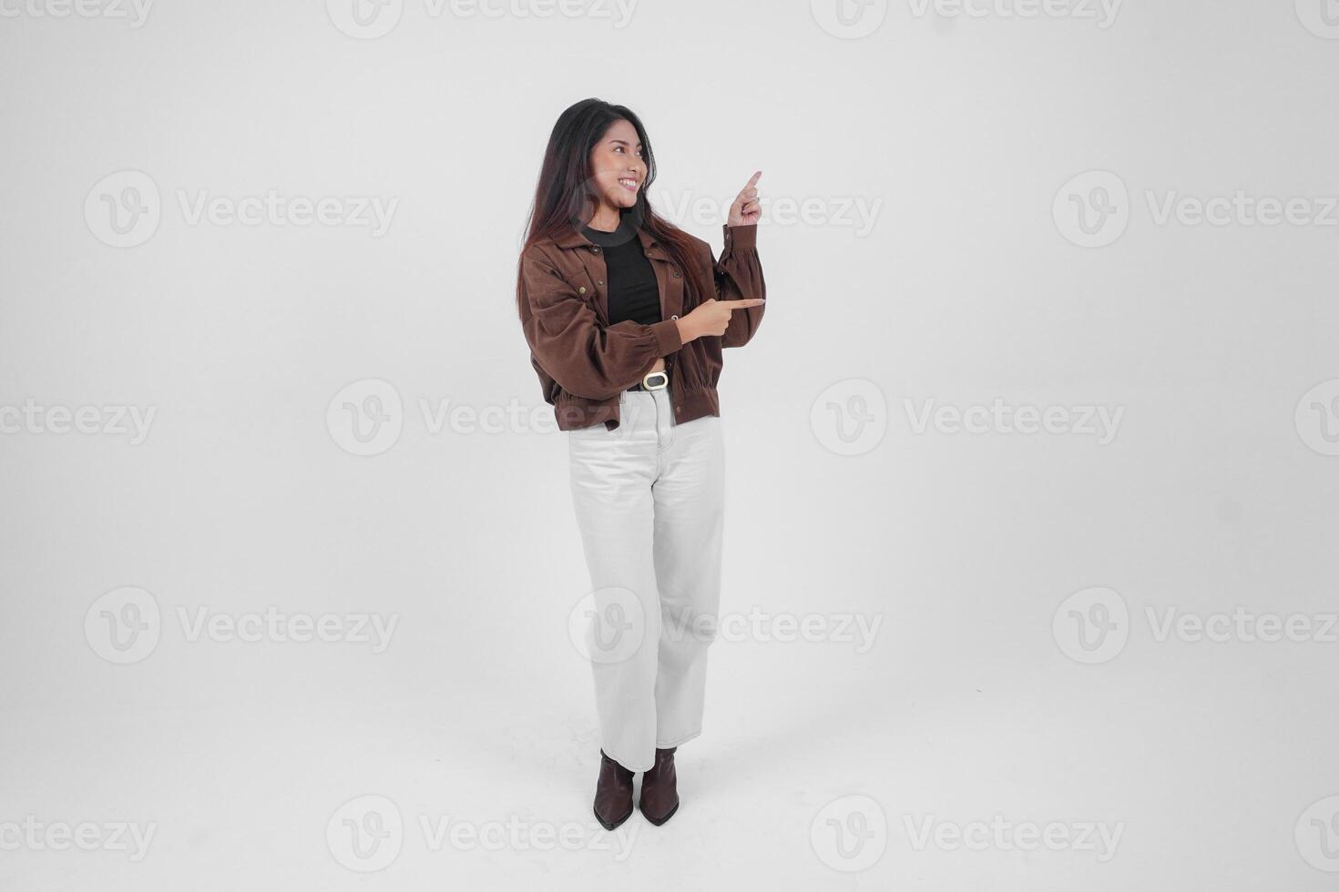 sorridente giovane asiatico ragazza indossare Marrone giacca è in piedi e puntamento per un' copia spazio accanto suo. foto