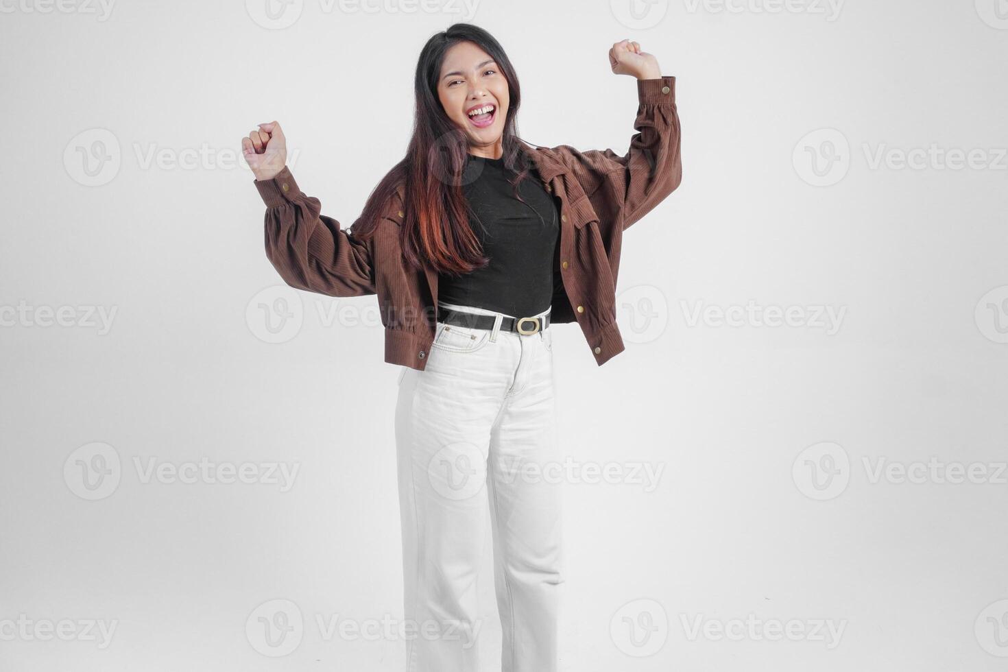 attivo asiatico ragazza è salto e raccolta mani su indossare Marrone giacca, isolato bianca colore sfondo foto