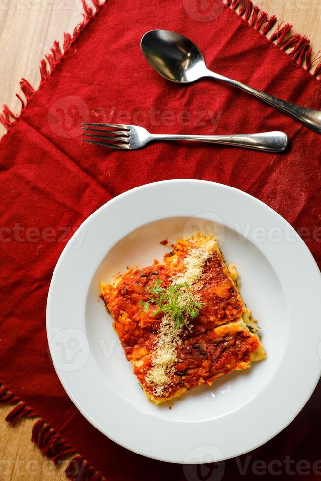speziato pomodoro e Manzo Lasagna servito nel piatto con forchetta e cucchiaio isolato su rosso tovagliolo superiore Visualizza di veloce cibo su tavolo foto