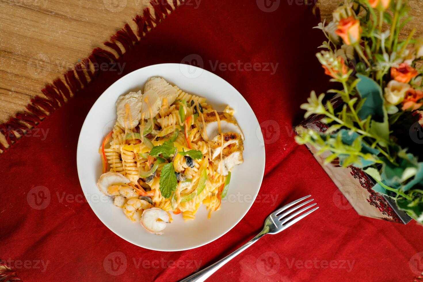 tropicale pasta insalata con mescolare carne oliva con gamberetto e gamberetto servito nel ciotola con fiori e forchetta isolato su rosso tovagliolo lato Visualizza di salutare verde cibo su tavolo foto