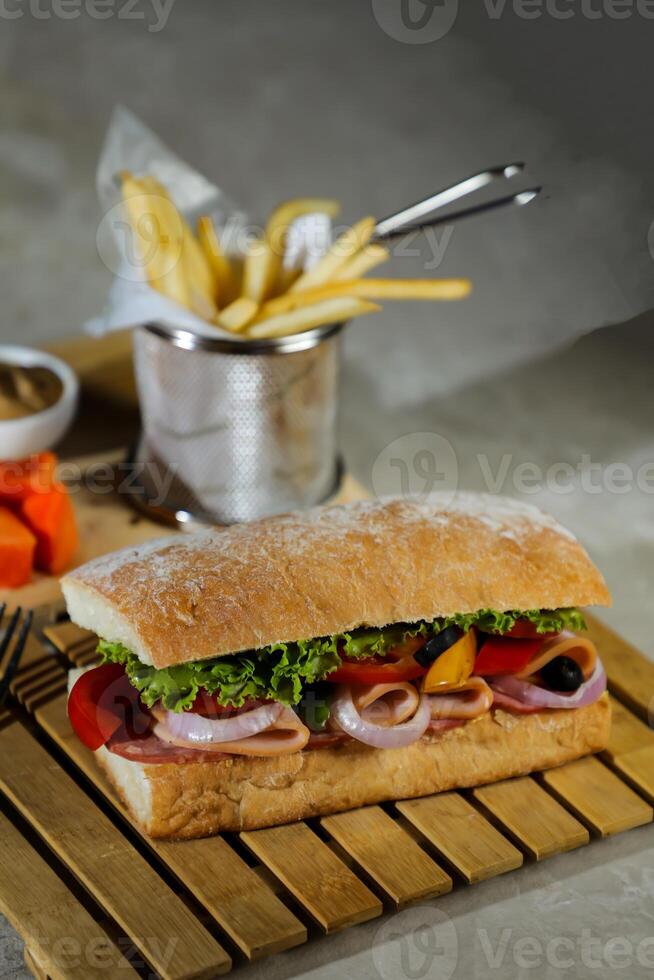 Ciabatta affumicato prosciutto Sandwich isolato su di legno con Maionese tuffo e francese patatine fritte secchio tavola lato Visualizza di italiano veloce cibo su grigio sfondo foto