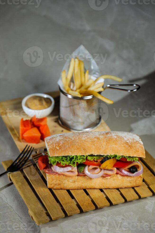 Ciabatta affumicato prosciutto Sandwich isolato su di legno con Maionese tuffo e francese patatine fritte secchio tavola lato Visualizza di italiano veloce cibo su grigio sfondo foto