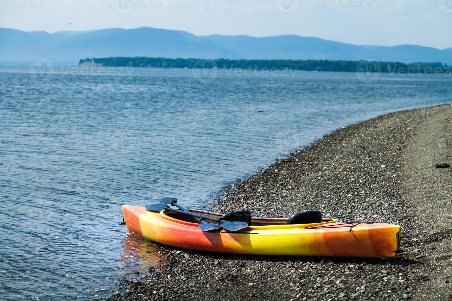 kayak arancione e giallo con remi in riva al mare foto