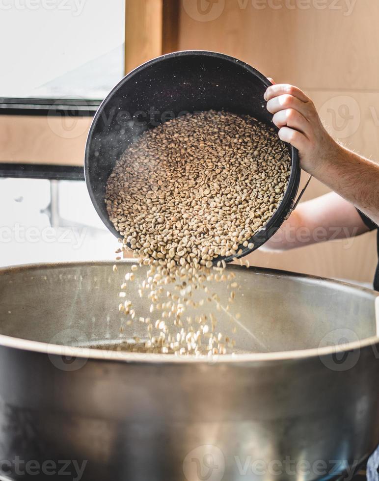 persona del raccolto che versa i chicchi di caffè crudo nella macchina per la torrefazione del caffè foto