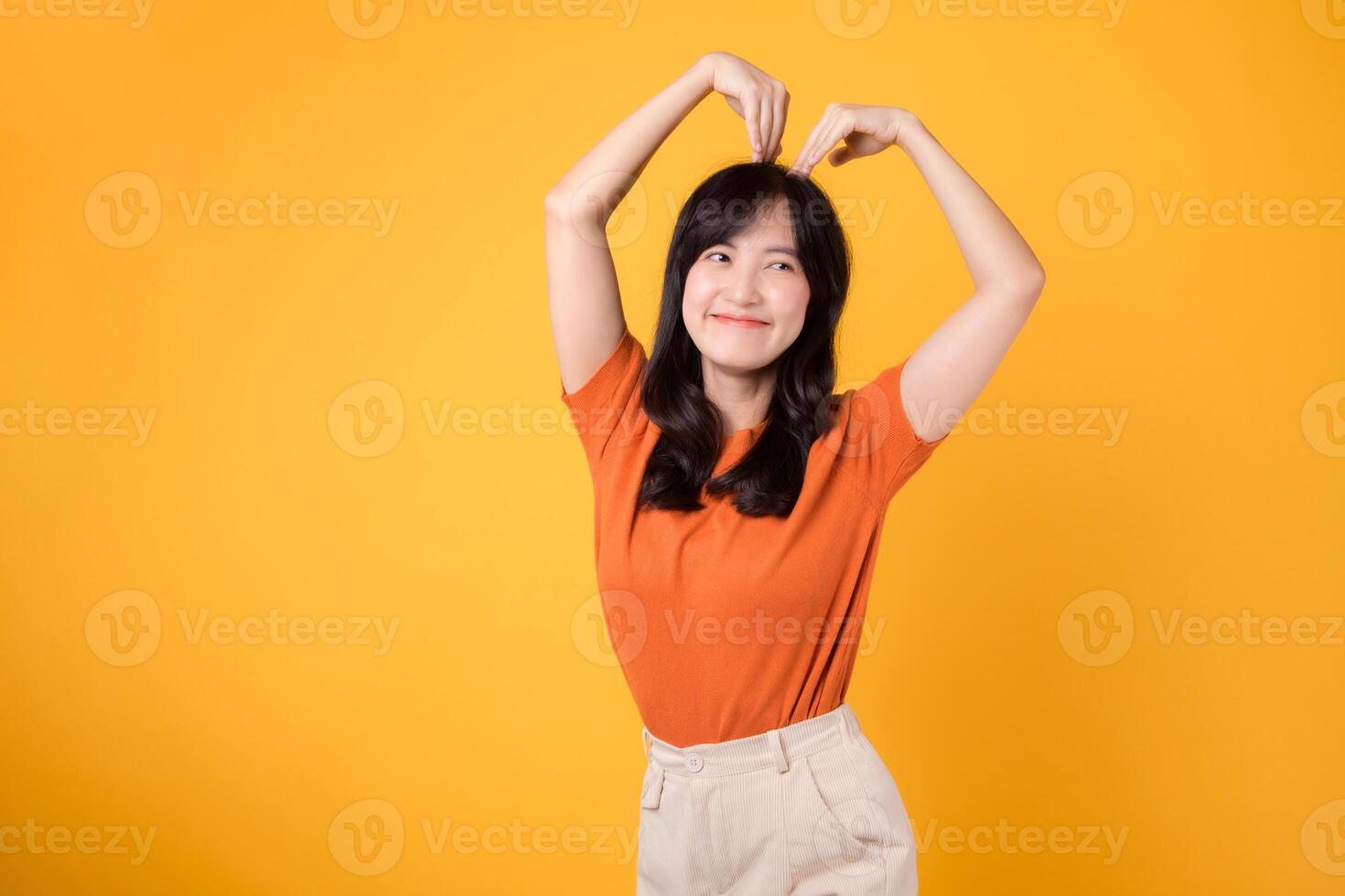 calore e autenticità brillare attraverso come un' allegro asiatico donna nel sua 30s abbraccia amore con un' a forma di cuore gesto e un infettivo Sorridi. foto