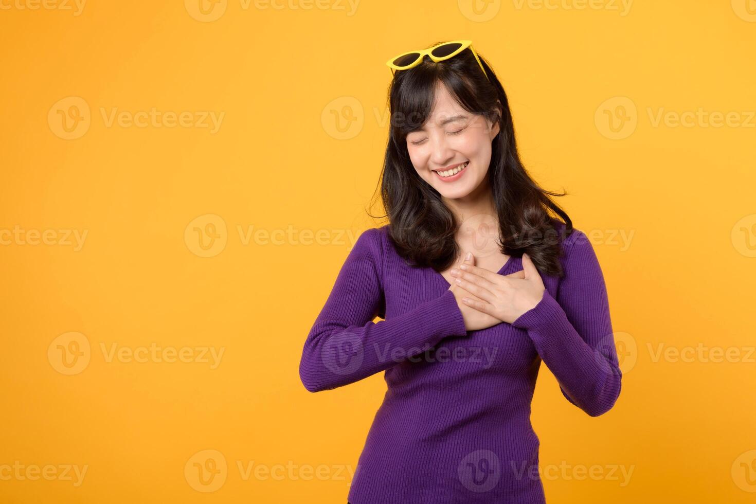 assistenza sanitaria e benessere con un asiatico giovane donna nel sua anni '30, indossare un' viola camicia. lei vetrine un' mano gesto su sua il petto contro un' giallo sfondo, incarnando il concetto di corpo benessere. foto