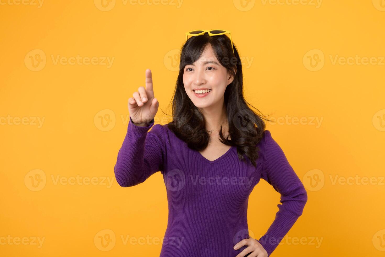 giovane asiatico donna 30s indossare viola camicia e occhiali da sole su testa contento Sorridi espressione toccante virtuale schermo isolato su giallo sfondo. tecnologia concetto. foto