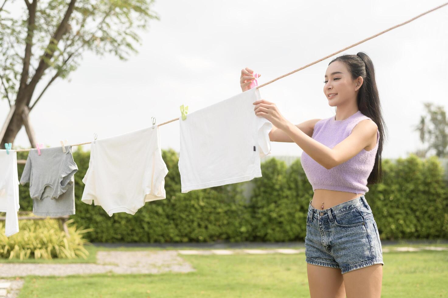 giovane asiatico donna sospeso lavanderia su lavaggio linea per essiccazione contro blu cielo all'aperto foto