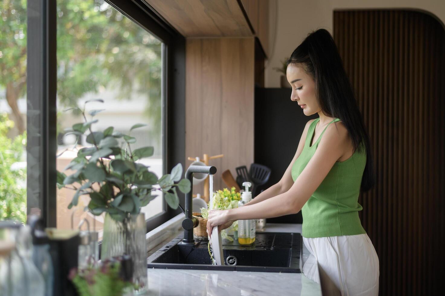 asiatico donna lavaggio piatti nel il cucina Lavello a casa foto