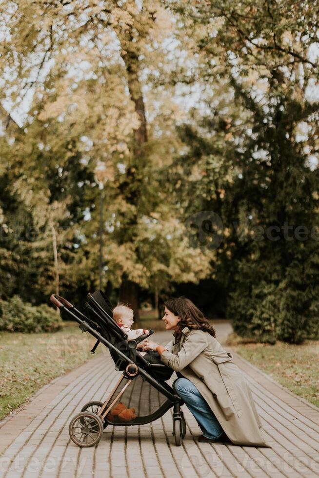 giovane donna con carino bambino ragazza nel bambino passeggino a il autunno parco foto