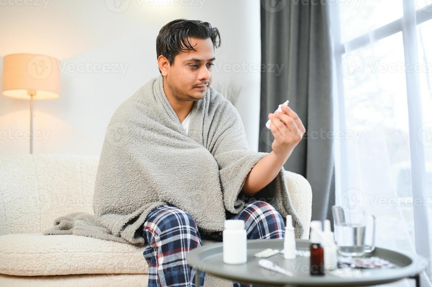 rinite, medicina e assistenza sanitaria concetto - malato indiano uomo nel coperta utilizzando nasale spray a casa foto