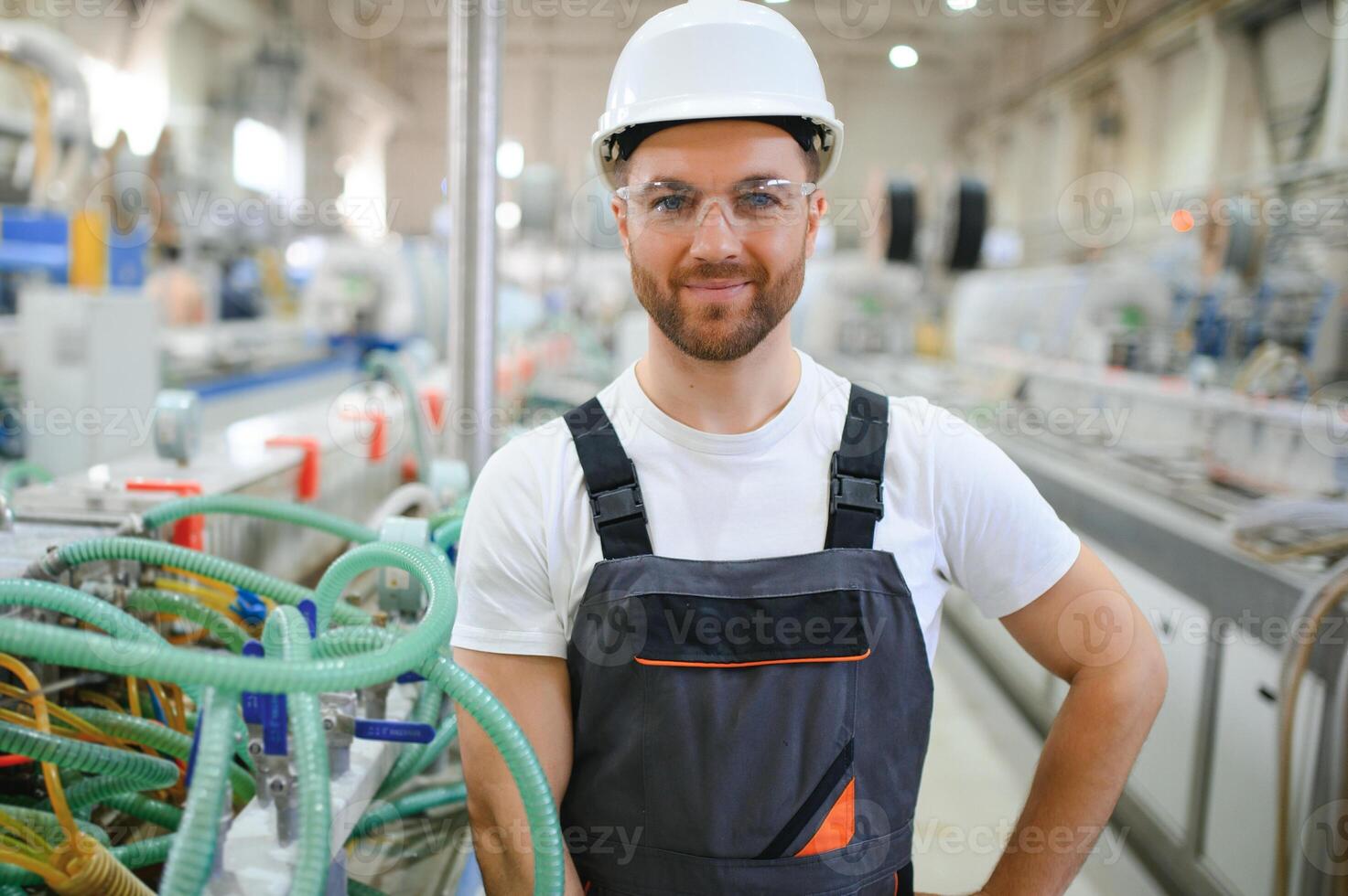 sorridente e contento dipendente. industriale lavoratore in casa nel fabbrica. giovane tecnico con difficile cappello foto