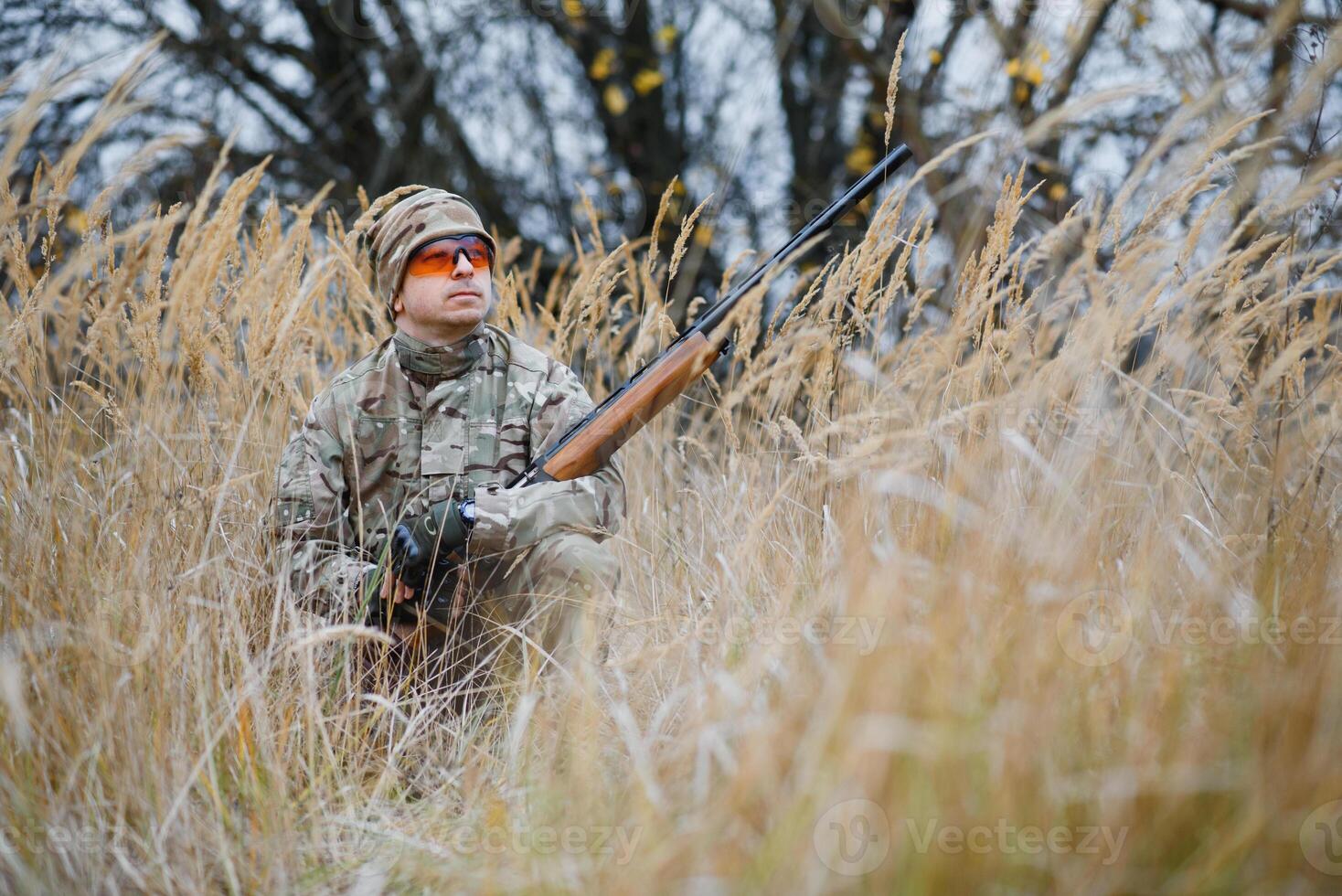 un' maschio cacciatore con un' pistola mentre seduta prende scopo a un' foresta. il concetto di un' riuscito caccia, un esperto cacciatore. a caccia il autunno stagione. il cacciatore ha un' fucile e un' a caccia uniforme foto