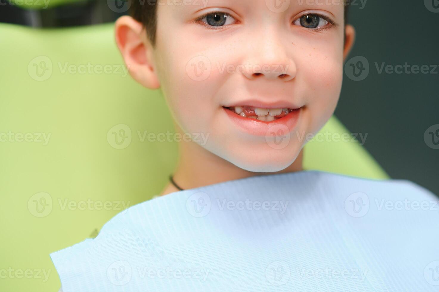 poco ragazzo si siede su dal dentista sedia nel bene umore dopo dentale procedure. giovane paziente con salutare denti foto