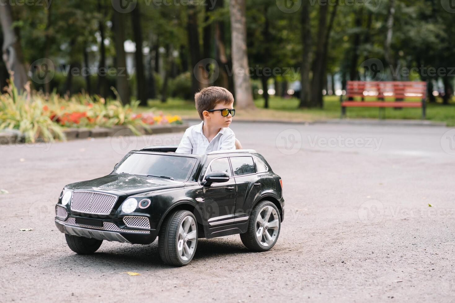 carino ragazzo nel equitazione un' nero elettrico auto nel il parco. divertente ragazzo cavalcate su un' giocattolo elettrico macchina. copia spazio. foto