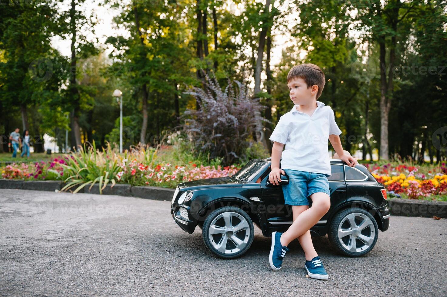 carino ragazzo nel equitazione un' nero elettrico auto nel il parco. divertente ragazzo cavalcate su un' giocattolo elettrico macchina. copia spazio. foto