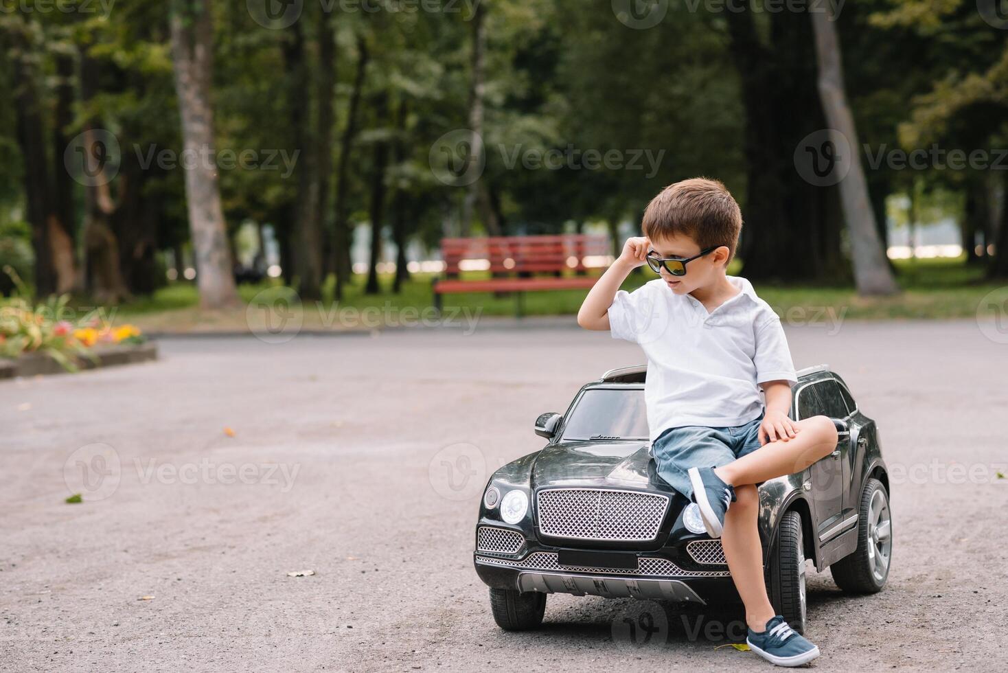 carino ragazzo nel equitazione un' nero elettrico auto nel il parco. divertente ragazzo cavalcate su un' giocattolo elettrico macchina. copia spazio. foto