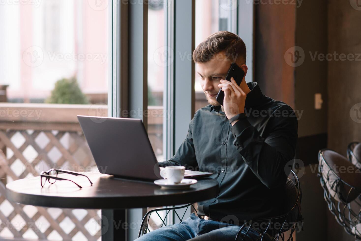 giovane uomo d'affari parlando su mobile Telefono mentre Lavorando su il computer portatile nel bar. foto