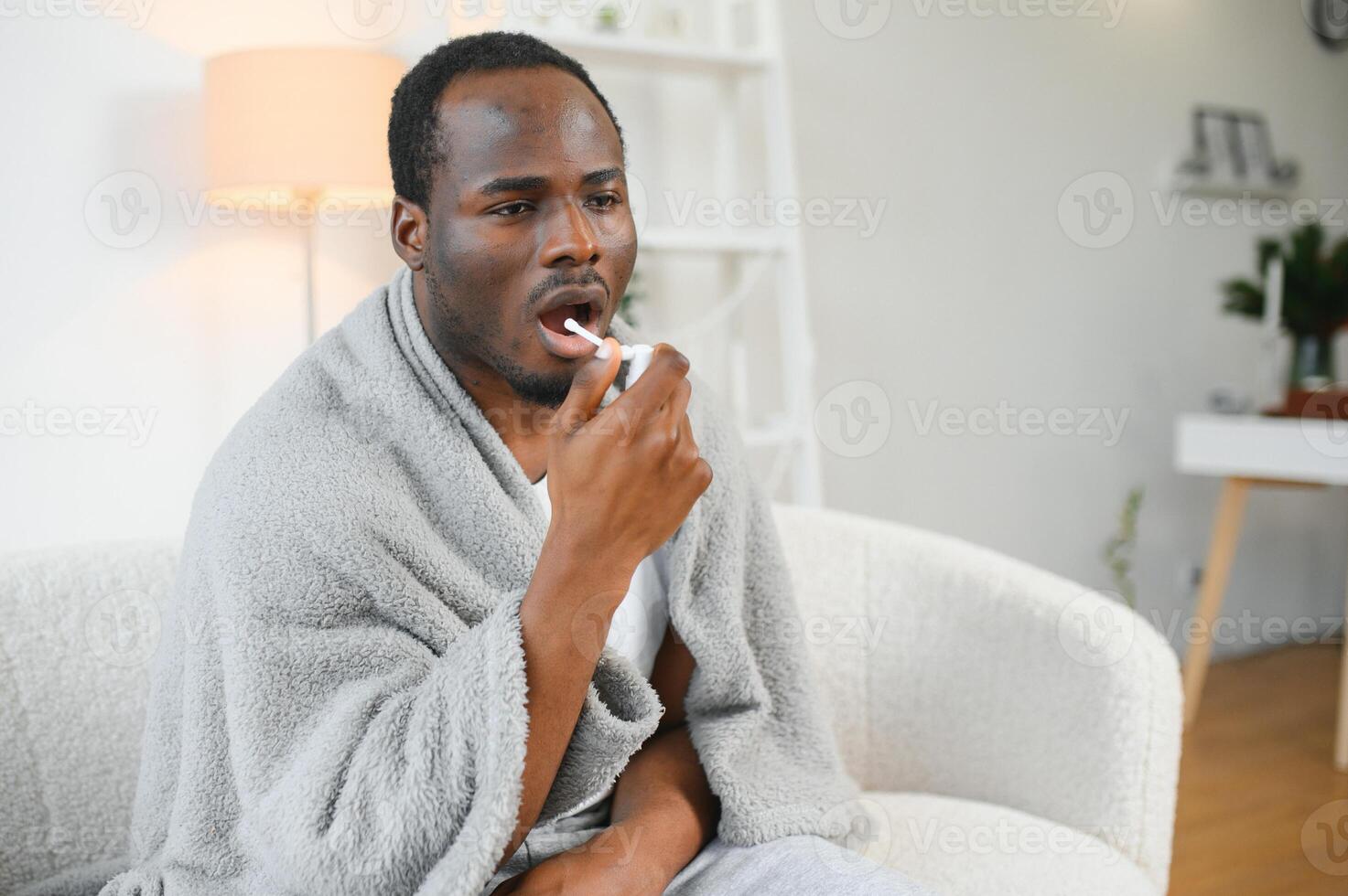 malato africano uomo utilizzando gola spray a casa foto