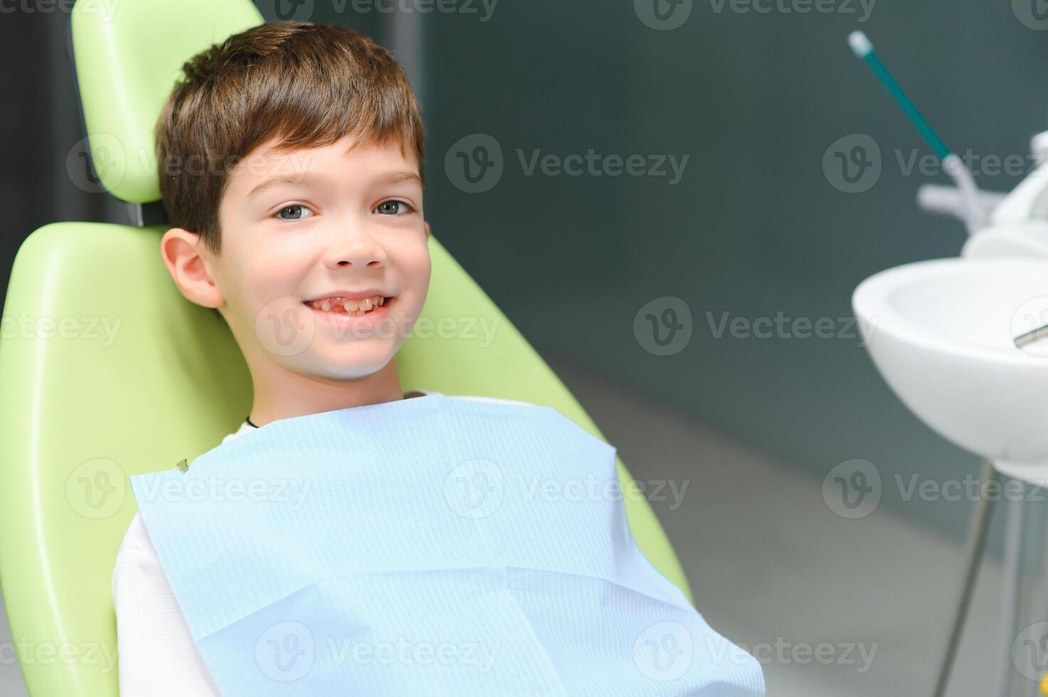 poco ragazzo si siede su dal dentista sedia nel bene umore dopo dentale procedure. giovane paziente con salutare denti foto