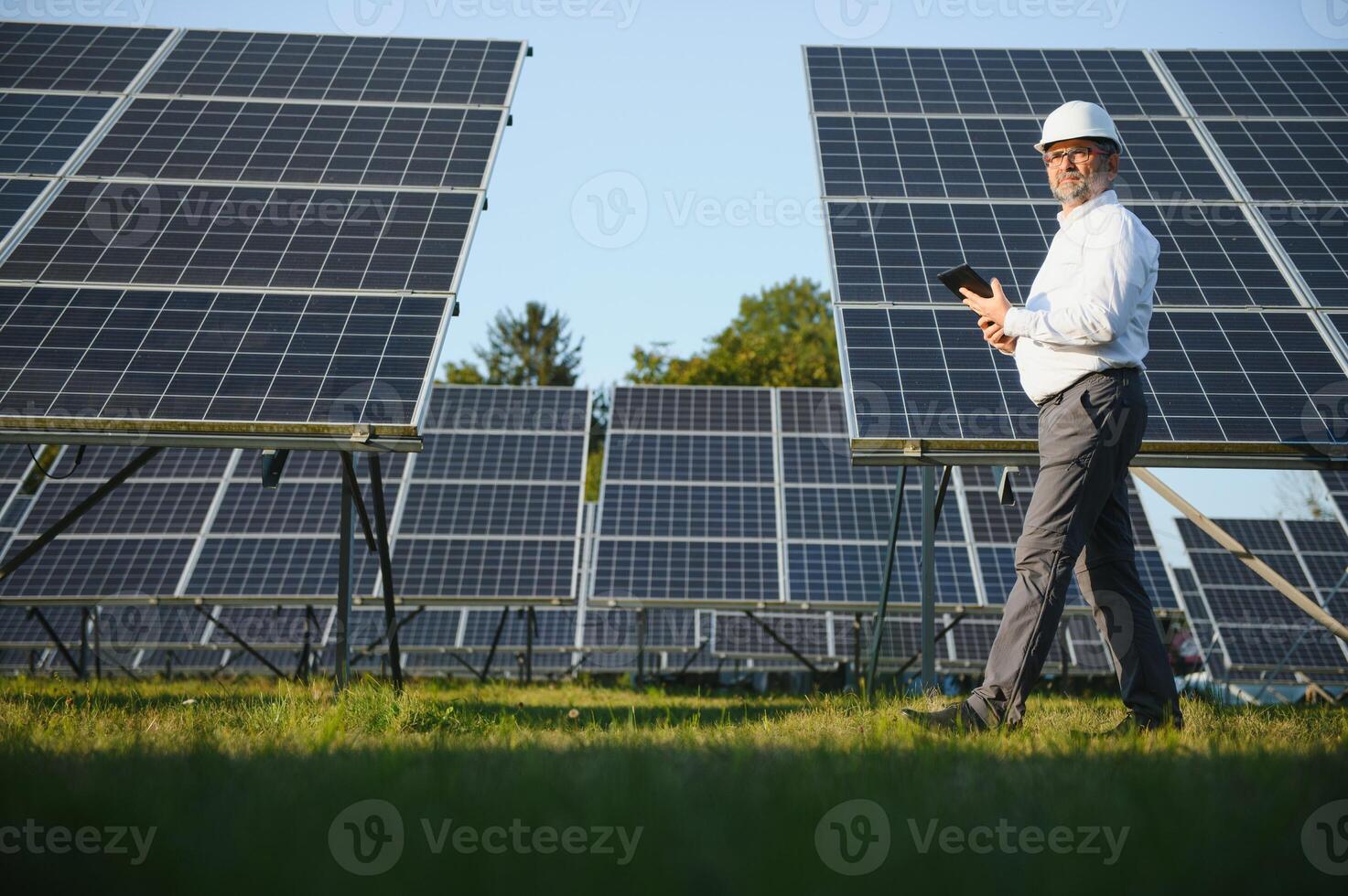 industriale anziano uomo ingegnere a piedi attraverso solare pannello campo per visita medica foto