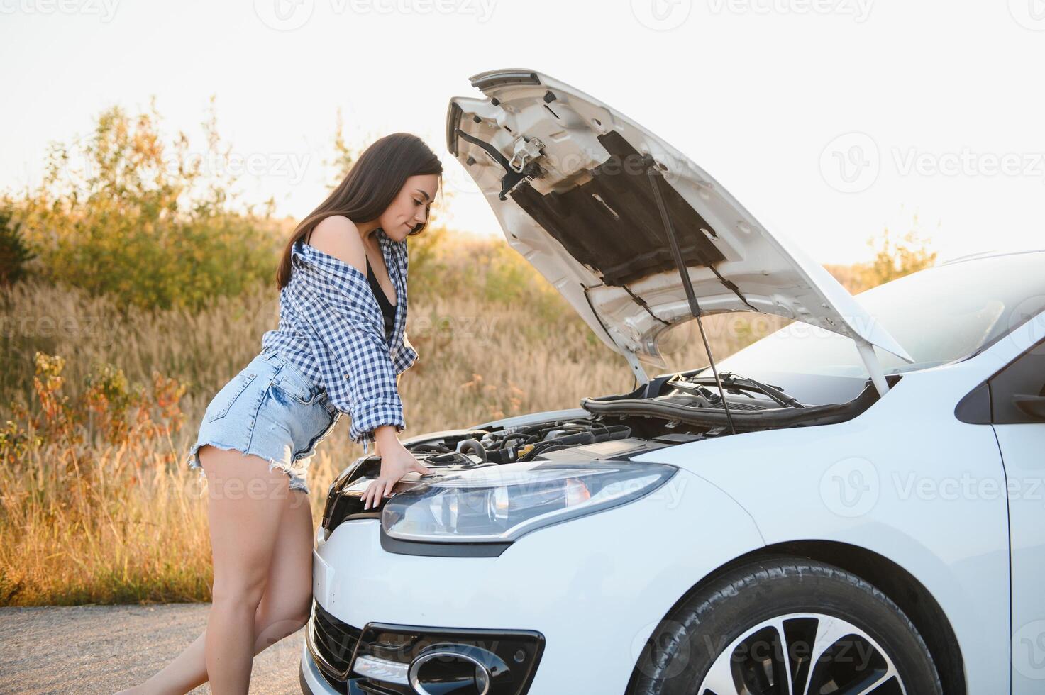 bellissimo sottile ragazza nel camicia e pantaloncini sembra nel Aperto auto cappuccio su un' strada foto