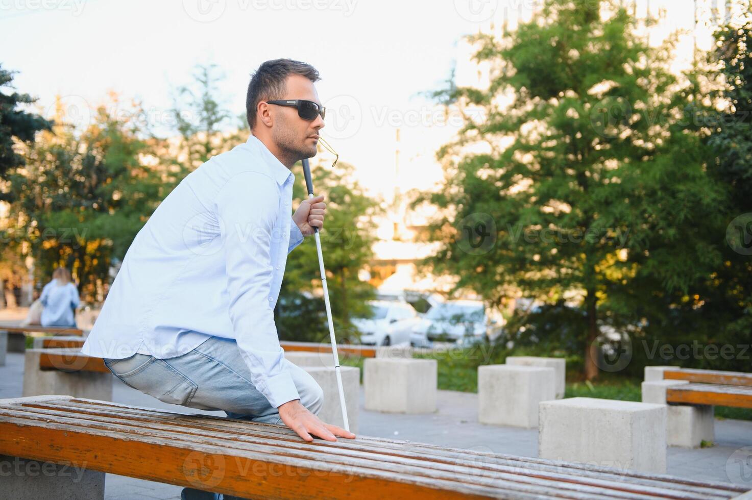 cieco uomo con un' a piedi bastone seduta su un' panchina a un' parco foto