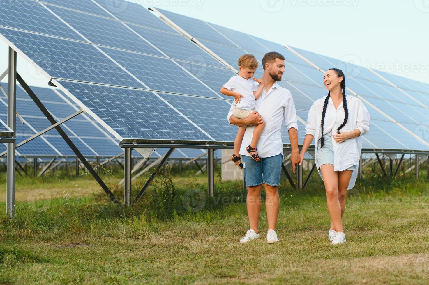 giovane famiglia di tre è accovacciato vicino fotovoltaico solare pannello, poco ragazzo e genitori. moderno famiglia concetto. il concetto di verde energia foto