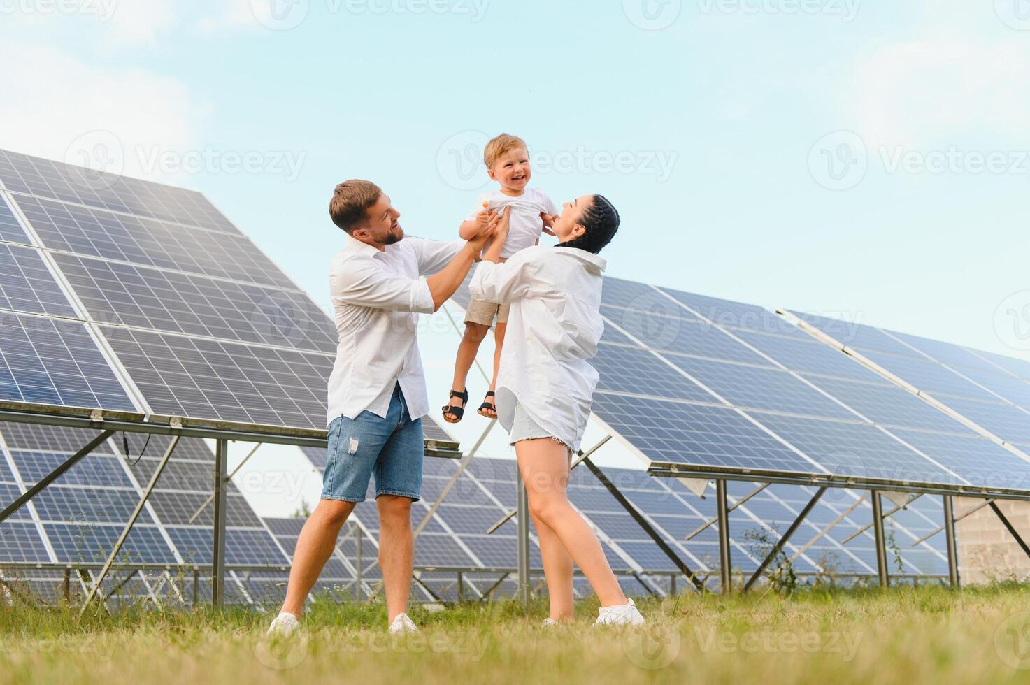 un' largo tiro di un' contento famiglia in piedi insieme e sorridente a telecamera con un' grande solare pannello nel sfondo foto