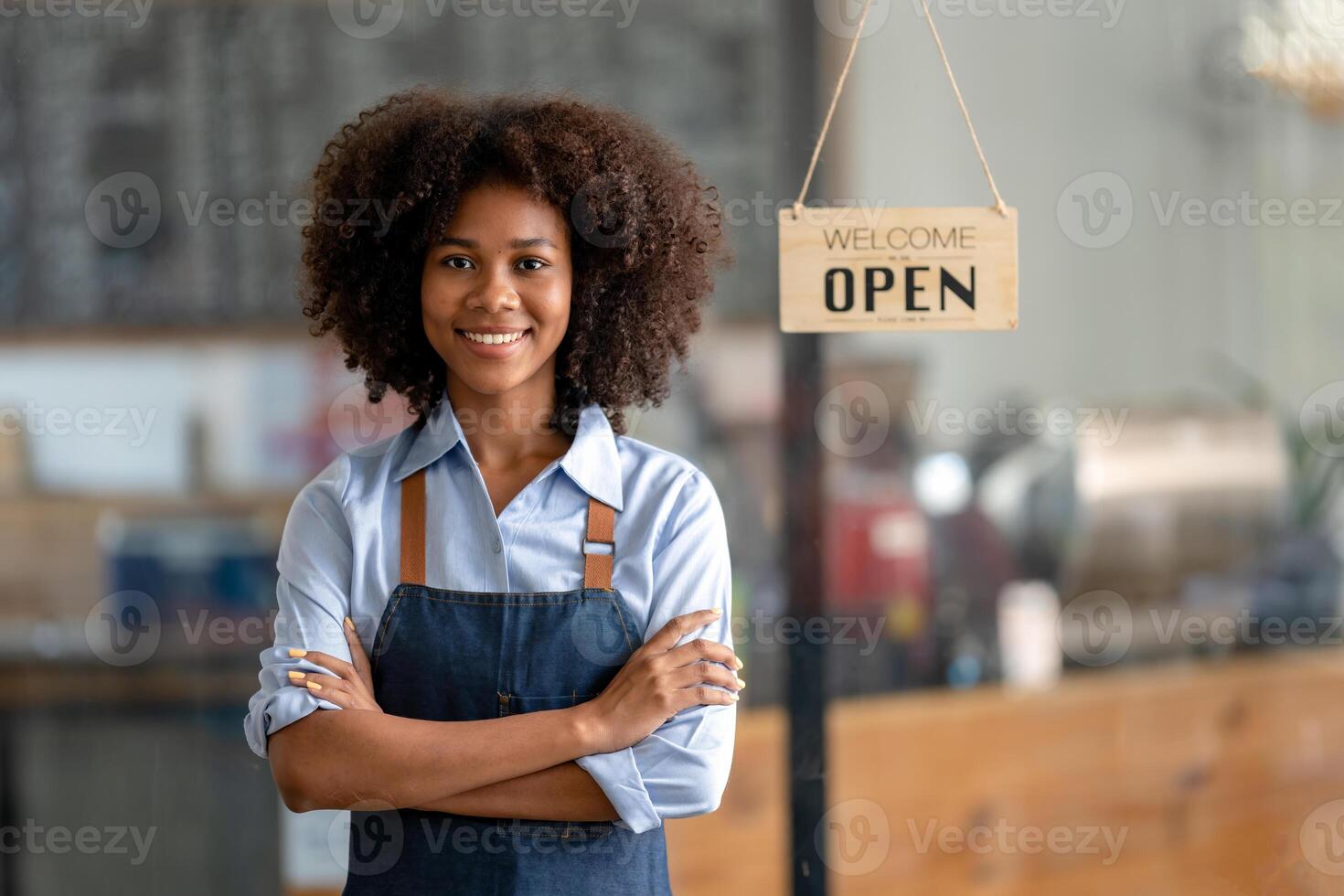 riuscito africano americano donna nel grembiule in piedi caffè negozio porta. contento piccolo attività commerciale proprietario. sorridente ritratto di imprenditore in piedi con copia spazio. foto