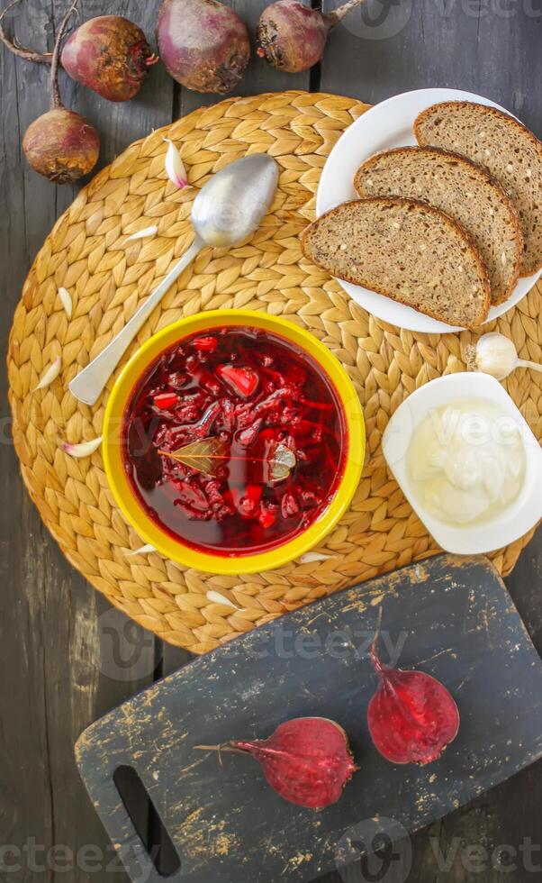 rosso tradizionale russo e ucraino borscht o barbabietola la minestra con acida crema, aglio e aromi nel un' giallo ceramica tazza su di vimini tovaglietta sfondo. foto