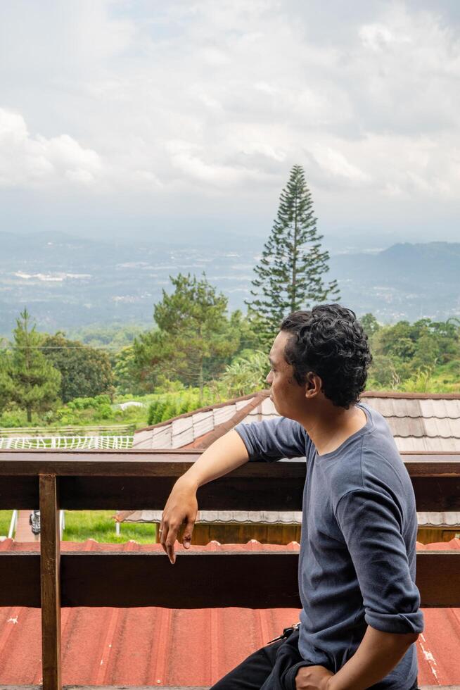 uomo seduta vicino recinto e guardare il paesaggio montagna. il foto è adatto per uso per calma goduto attività, tempo libero attività e parco sfondo.