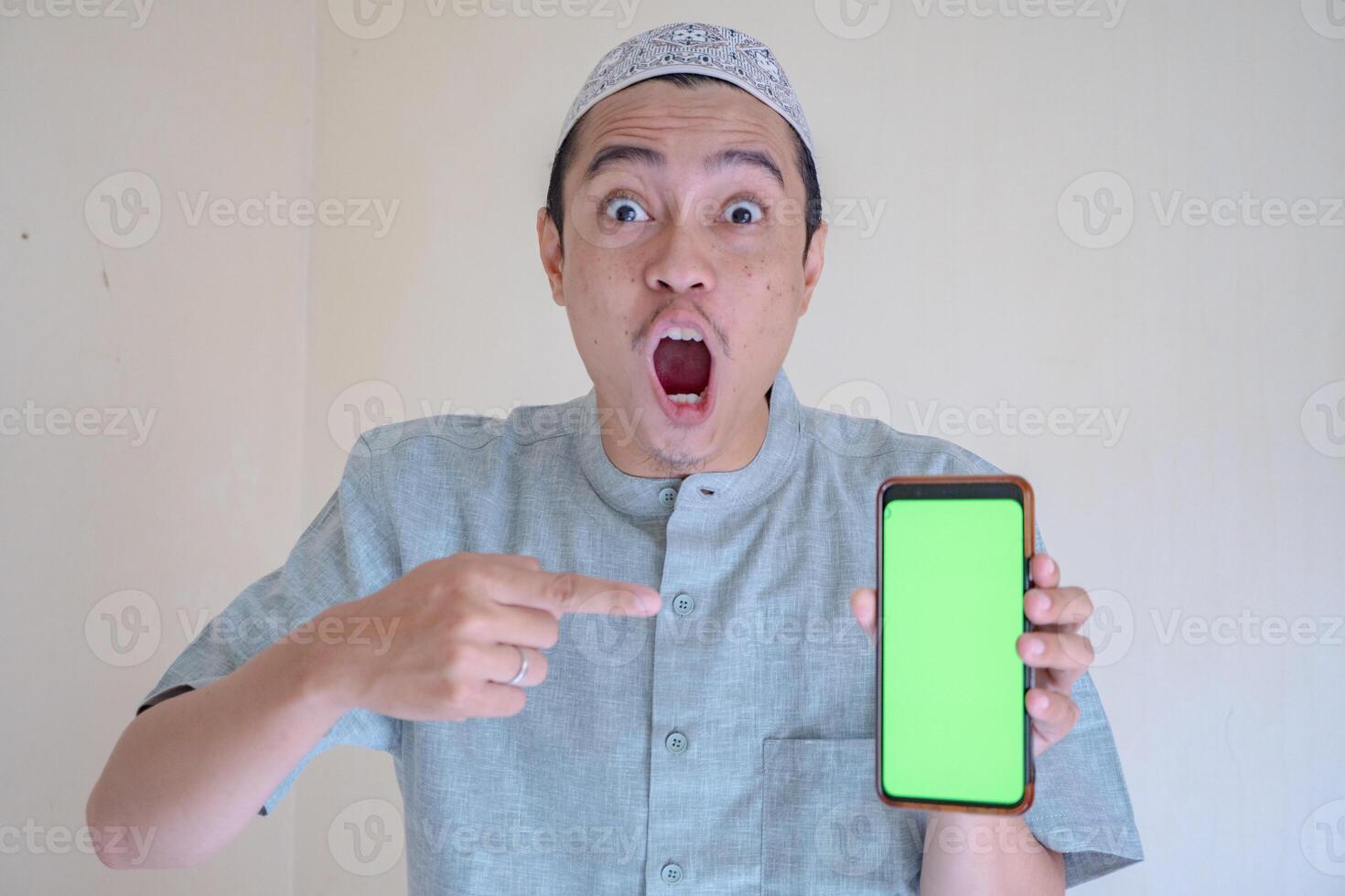 musulmano asiatico uomo sorpreso gesto mostrare il schermo verde su smartphone quando Ramadan celebrazione. il foto è adatto per uso per Ramadhan manifesto e musulmano soddisfare media.