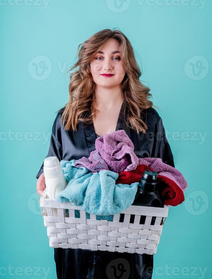 casalinga felice che tiene un cesto di vestiti pronti per il bucato isolato su sfondo blu foto