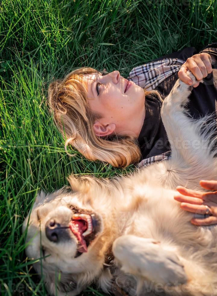 bella donna caucasica sdraiata sull'erba con il suo cane golden labrador retriever in un parco al tramonto foto