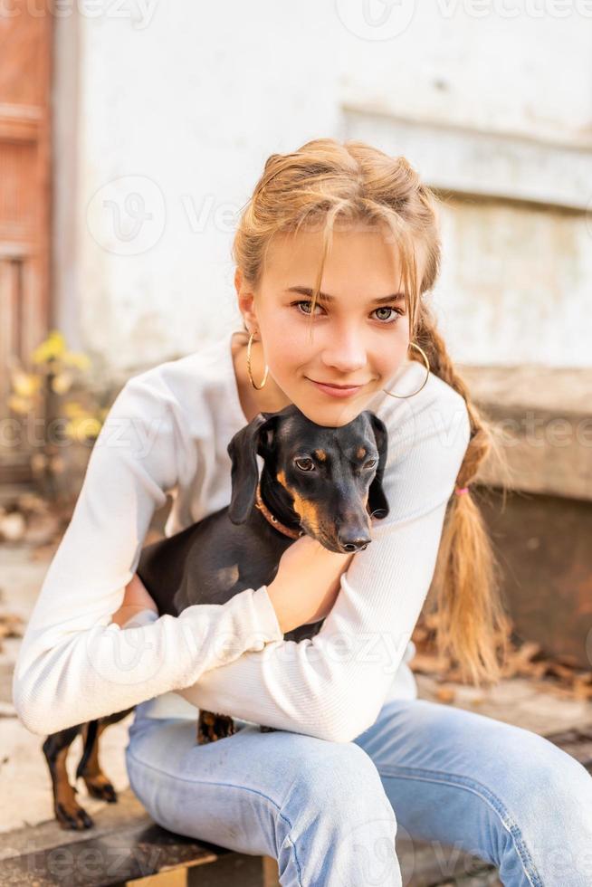 ragazza adolescente che abbraccia il suo cane bassotto all'aperto foto