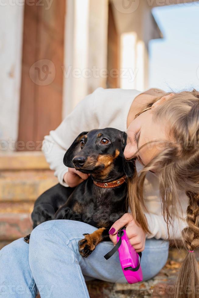 ragazza adolescente che abbraccia il suo cane bassotto all'aperto seduto sulle scale foto