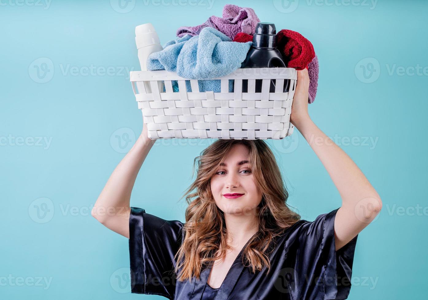 casalinga felice che tiene un cesto di vestiti pronti per il bucato sulla sua testa isolato su sfondo blu foto