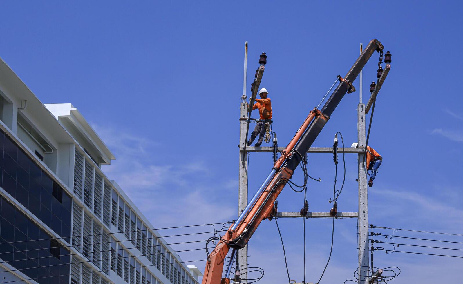 Due elettricisti con gru camion siamo Lavorando per installare elettrico trasmissione su energia poli con edificio contro blu cielo sfondo foto