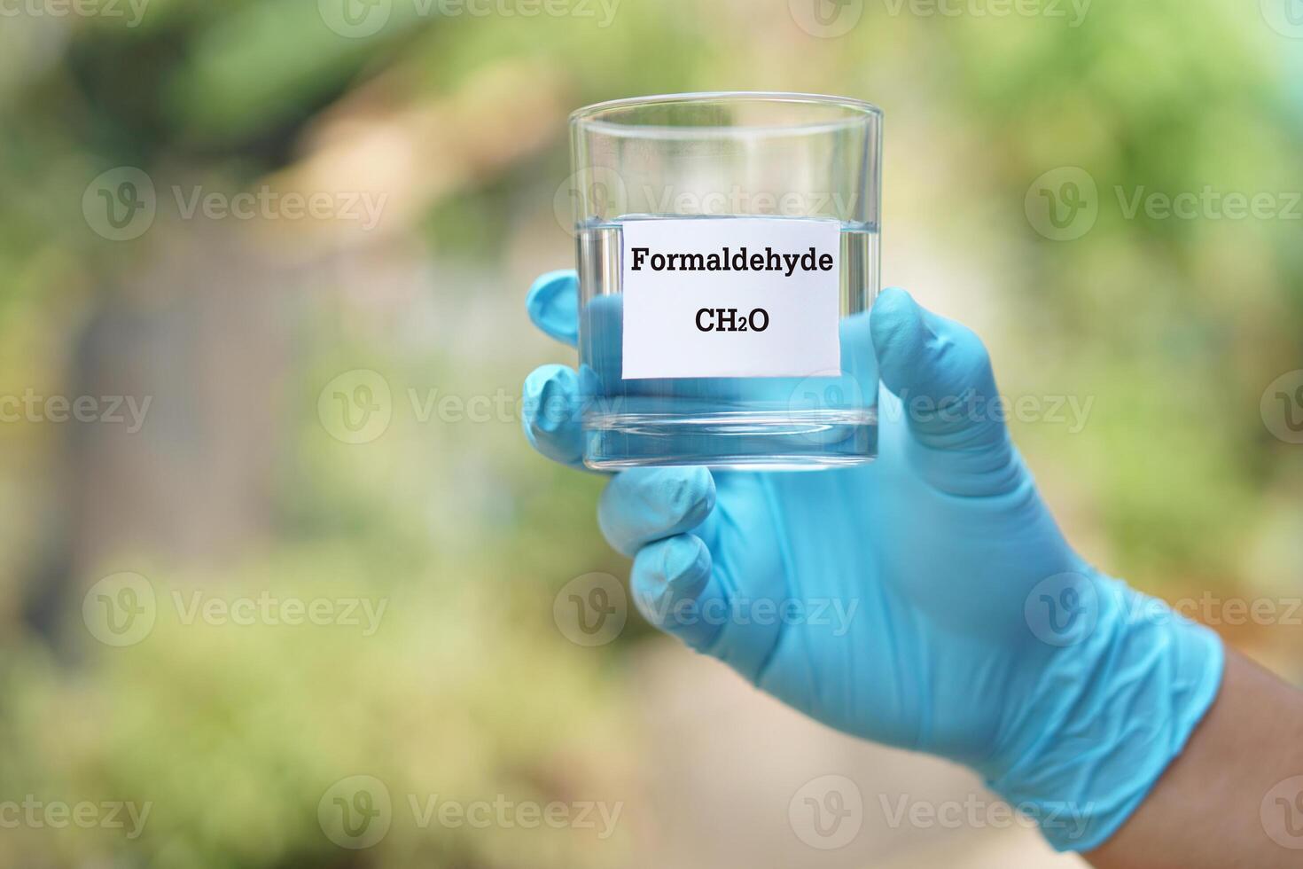 vicino su mano indossare blu guanto, detiene test bicchiere di formaldeide liquido con molecolare formula ch2o. concetto, chimico sostanza, incolore, tossico, odore forte e infiammabile foto