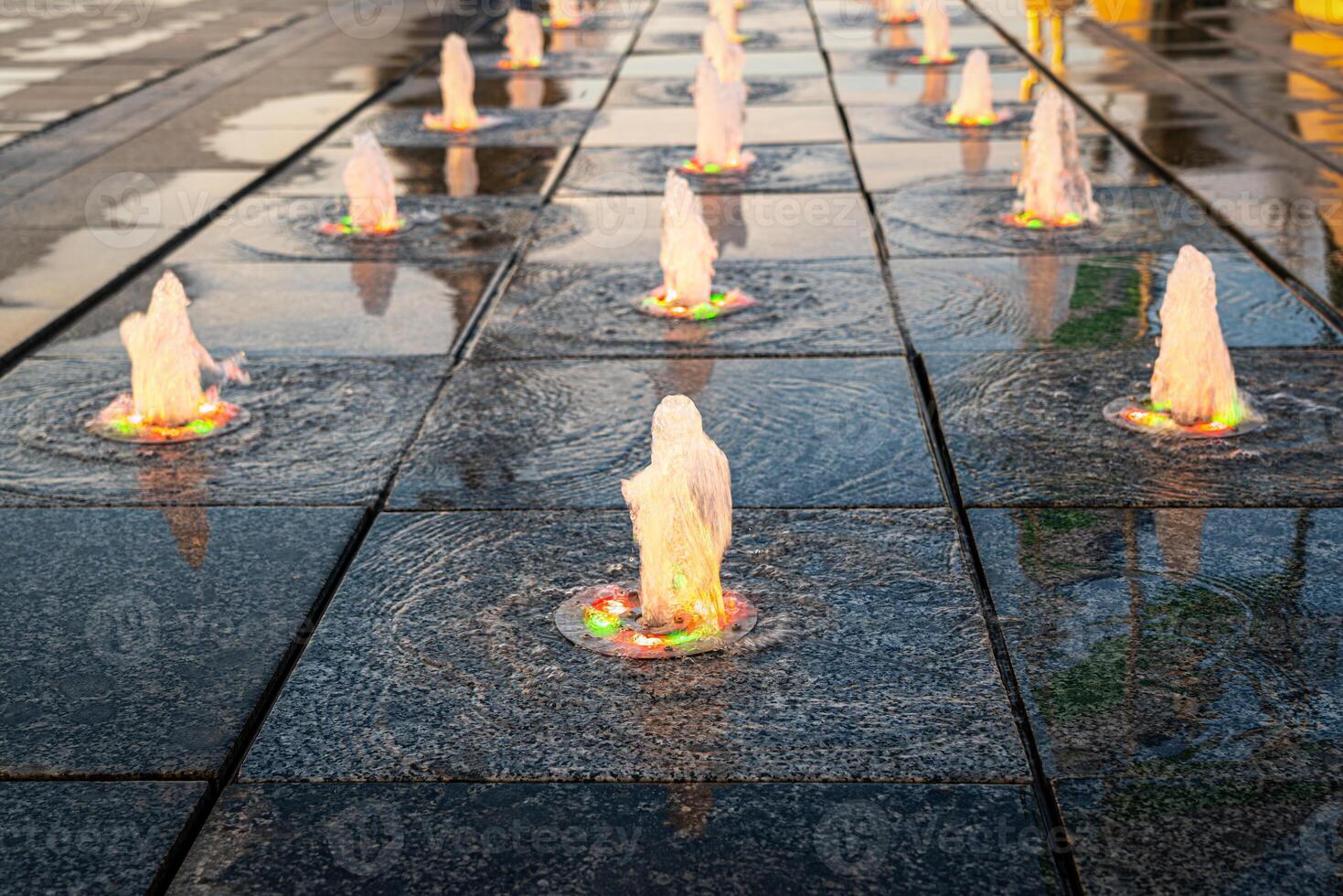 piccolo fontane su il marciapiede, illuminato di luce del sole a tramonto o Alba a estate. foto