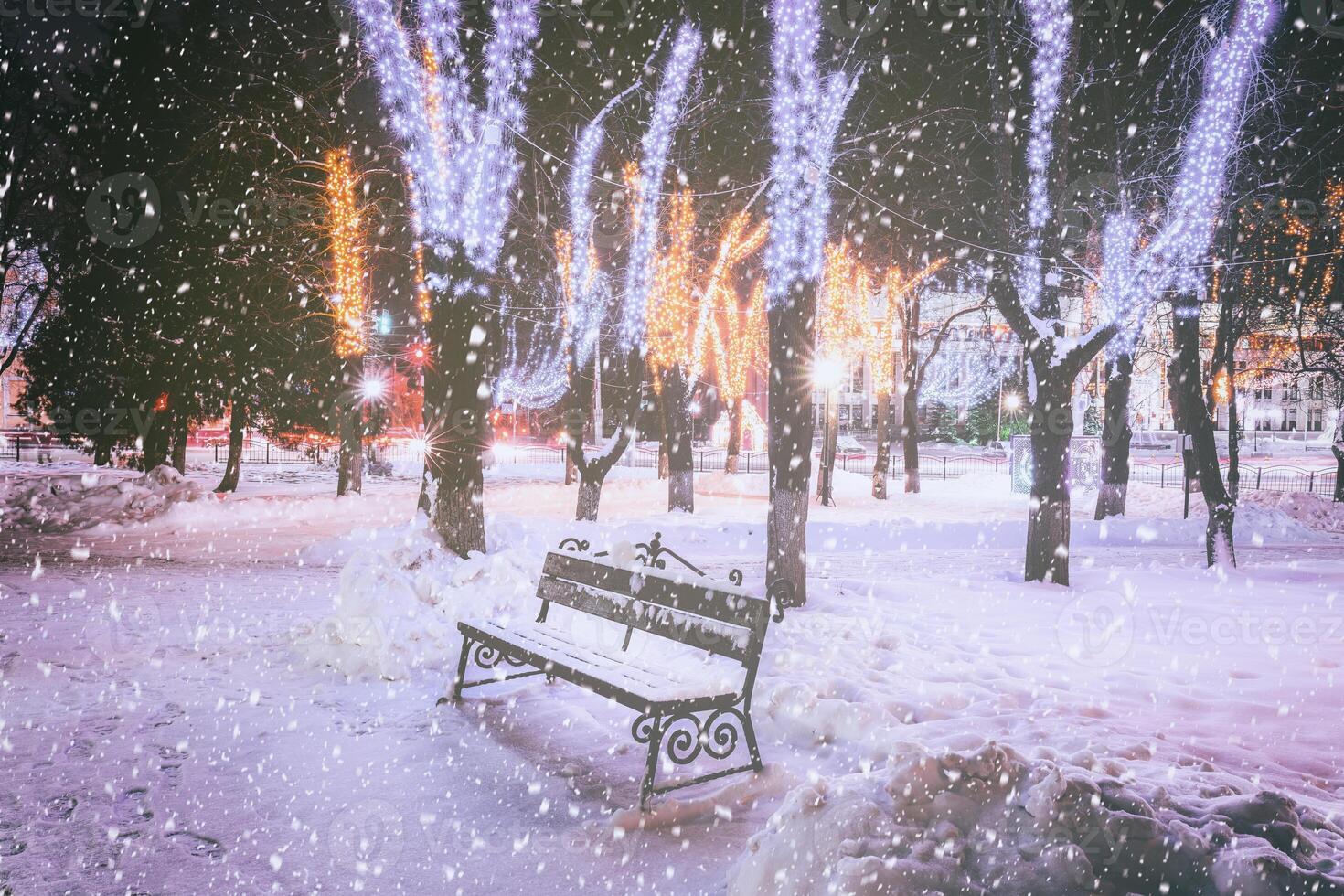 nevicata nel un' inverno parco a notte con decorazioni, raggiante lanterne, marciapiede coperto con neve e alberi. Vintage ▾ film estetico. foto