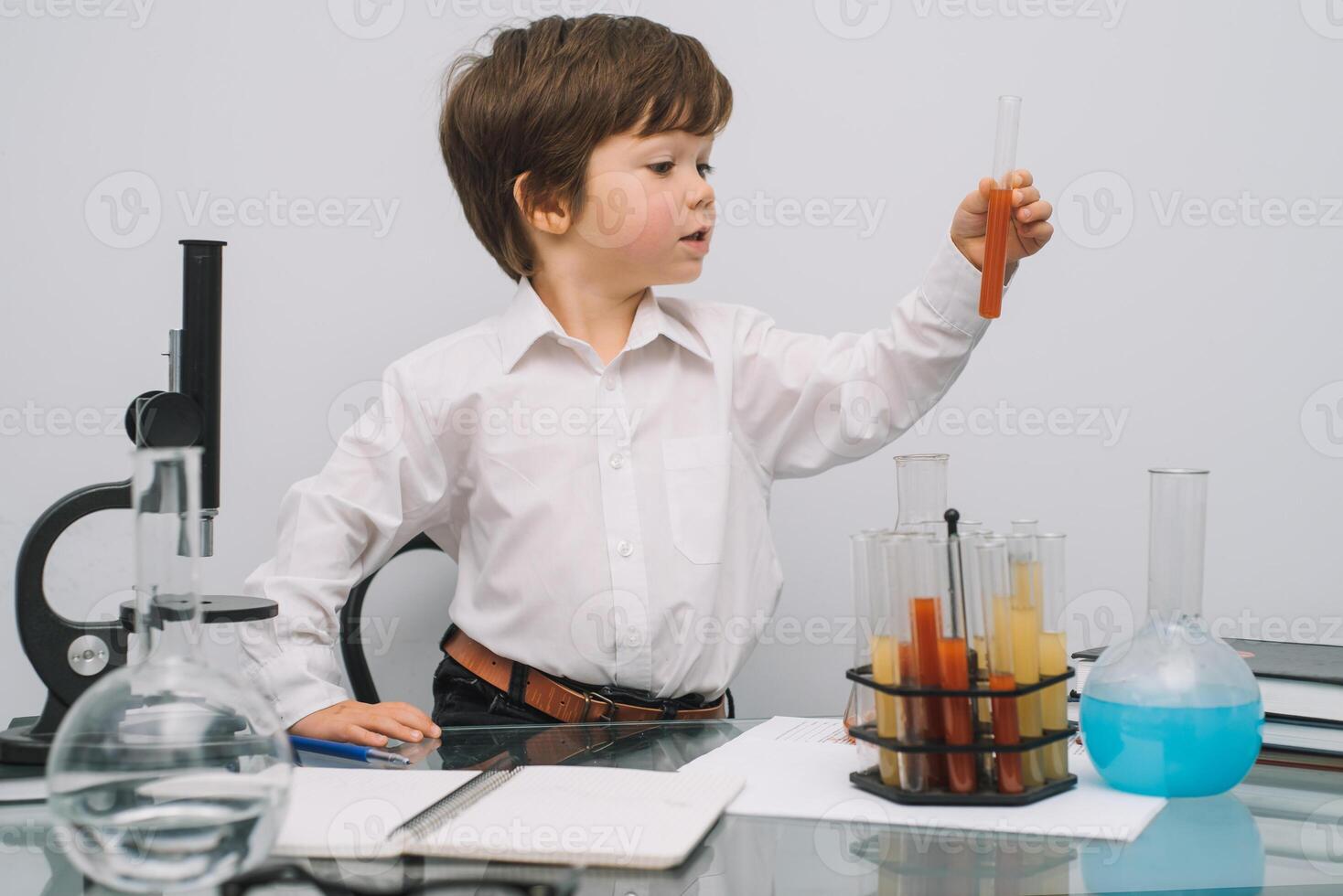 il ragazzo con un' microscopio e vario colorato fiaschi su un' bianca sfondo. un' ragazzo fare esperimenti nel il laboratorio. esplosione nel il laboratorio. scienza e formazione scolastica foto