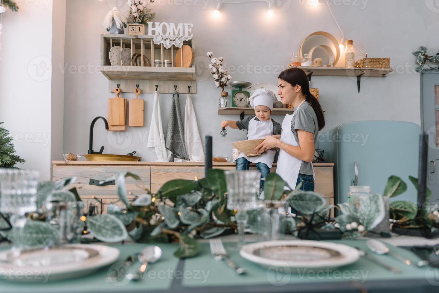 giovane contento mamma e sua bambino cucinare biscotti a casa nel il cucina. Natale fatti in casa Pan di zenzero. carino ragazzo con madre nel bianca uniforme e cappello cucinato cioccolato biscotti foto